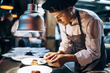 Seitenansicht eines Mannes mit Hut, der in einer Restaurantküche Essen serviert - ADSF39566