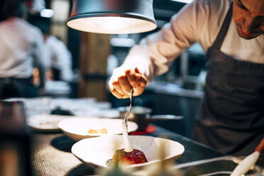 Crop professionellen Koch gießen weiße Soße auf Gericht in eleganten Teller arbeiten auf Restaurant Küche - ADSF39567