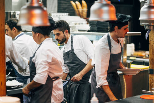 Männer mit Hüten und Schürzen, die im Team arbeiten und in der Küche köstliche Speisen servieren - ADSF39575