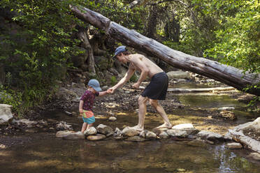Mann hilft Sohn beim Überqueren eines Baches im Wald - ACTF00264