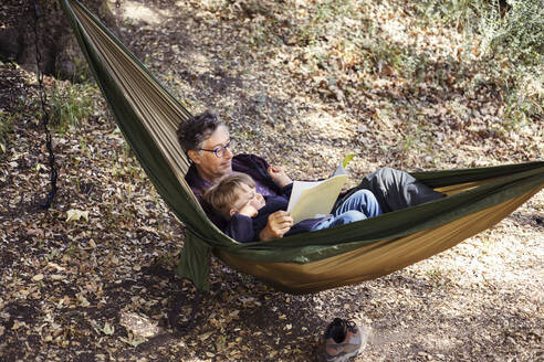 Großvater liest Buch für Enkel auf Hängematte im Wald liegend - ACTF00270