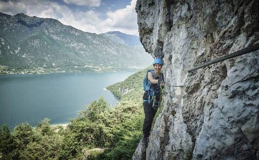 Happy woman climbing mountain with Lake Idro in background - DIKF00737