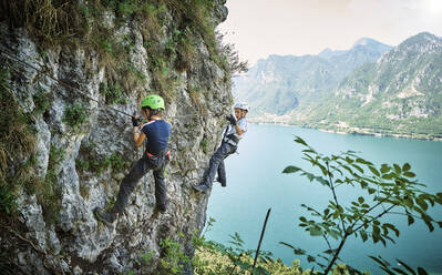 Girl with brother climbing mountain with Lake Idro in background - DIKF00740