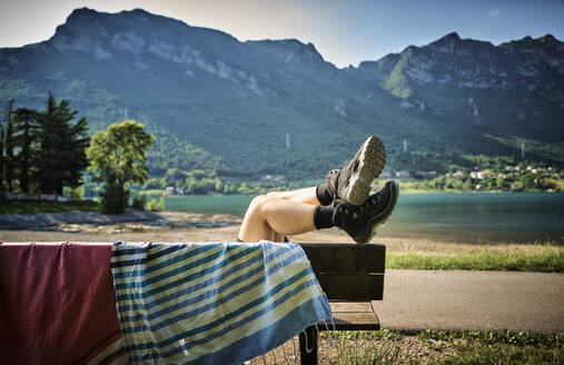 Legs of woman wearing hiking boots relaxing on bench with towel - DIKF00747