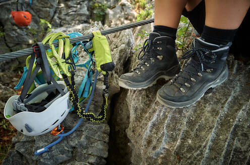 Legs of woman wearing hiking boots by climbing equipment rock - DIKF00748