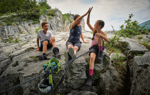 Boy looking at mother giving high five to girl on rock - DIKF00751