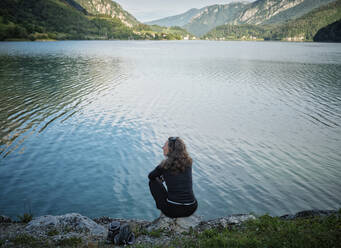 Mature woman sitting on rock at lakeshore - DIKF00760