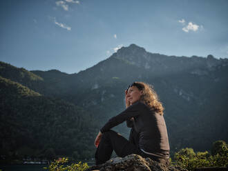 Lächelnde reife Frau sitzt auf einem Felsen - DIKF00768