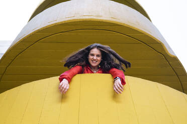 Glückliche junge Frau blickt aus gelbem Gebäude - AMWF00862