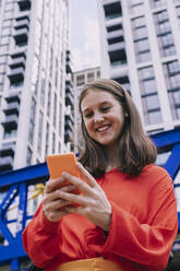 Glückliche Frau mit Smartphone vor einem Gebäude - AMWF00869