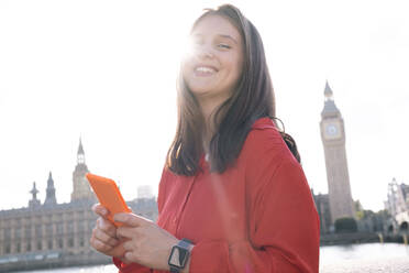 Happy young woman holding smart phone in city - AMWF00881