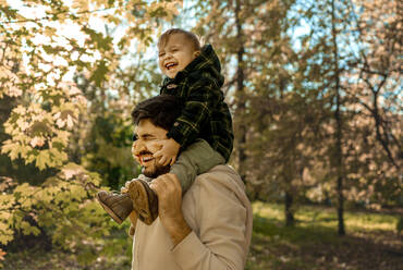 Glücklicher Vater trägt seinen Sohn im Park auf den Schultern - ANAF00202