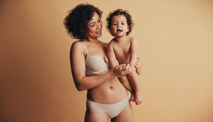 Happy woman with her baby. Loving mother carrying her child against brown studio background. - JLPSF10366