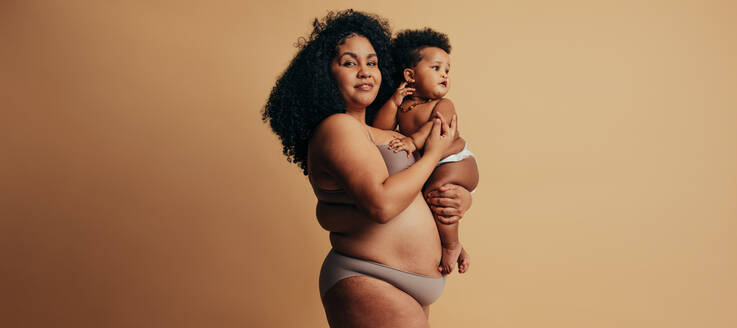 Gesunde Frau, die ihr Baby trägt. übergroße Mutter mit Kind auf braunem Hintergrund. - JLPSF10374