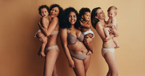 Gruppe von Müttern mit Babys. Frauen mit postpartalen Körpern, die ihre Kinder tragen, schauen in die Kamera und lächeln. - JLPSF10385
