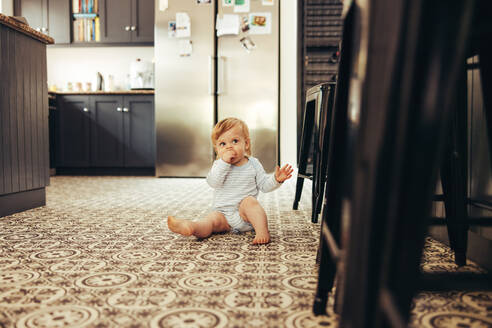 Baby sitzt auf dem Boden und isst etwas. Süßes Kind in der Küche zu Hause. - JLPSF10404