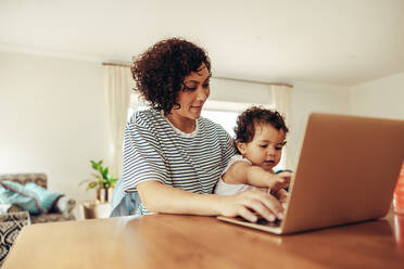 Mother and child sitting at table working on laptop computer. Woman with baby using laptop, working from home. - JLPSF10407