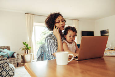 Frau Freiberufler mit Handy und Laptop mit ihrem Baby auf dem Schoß zu Hause sitzen. Working Mutter zu Hause mit Baby. - JLPSF10408