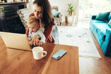 Woman sitting with a baby and using laptop. Working mother with her baby at home. - JLPSF10409