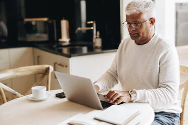 Älterer Geschäftsmann tippt auf einem Laptop, während er in seinem Büro zu Hause sitzt. Älterer Geschäftsmann sendet E-Mails und macht Geschäftspläne, während er von zu Hause aus arbeitet. - JLPSF10410