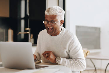 Glücklicher älterer Geschäftsmann, der während eines virtuellen Meetings in seinem Heimbüro fröhlich lacht. Älterer Geschäftsmann, der eine Videokonferenz mit seinen Kollegen abhält, während er von zu Hause aus arbeitet. - JLPSF10415