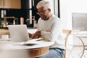 Cheerful senior businessman attending a virtual meeting in his home office. Mature businessman having a video conference with his colleagues while working from home. - JLPSF10416