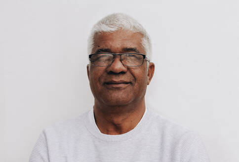 Confident senior man looking at the camera while standing against a white background. Portrait of a mature man wearing eyeglasses. - JLPSF10463