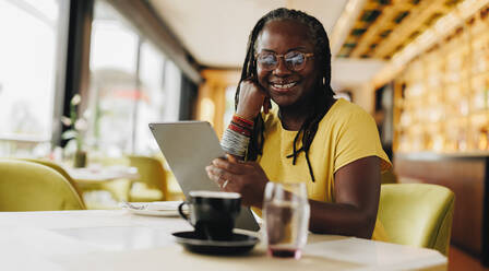 Glückliche Geschäftsfrau, die in die Kamera lächelt, während sie ein digitales Tablet in einem Café hält. Selbstständige ältere Frau, die in einem Café freiberufliche Online-Arbeiten erledigt. - JLPSF10481