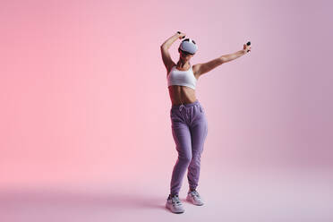 Junge Frau genießt eine Virtual-Reality-Erfahrung in einem Studio. Glückliche junge Frau tanzt, während sie ein Virtual-Reality-Headset trägt. Frau hat Spaß beim Erforschen der 3D-Technologie. - JLPSF10614