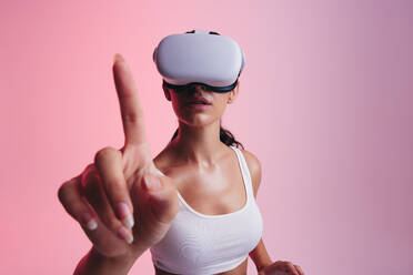 Frau interagiert mit virtueller Realität in einem Studio. Junge Frau berührt mit ihrem Finger den virtuellen Raum, während sie ein Virtual-Reality-Headset trägt. Frau erkundet 3D-Technologie in einem Studio. - JLPSF10623