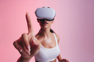 Frau interagiert mit virtueller Realität in einem Studio. Junge Frau berührt mit ihrem Finger den virtuellen Raum, während sie ein Virtual-Reality-Headset trägt. Frau erkundet 3D-Technologie in einem Studio. - JLPSF10623