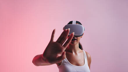 Eine Spielerin interagiert mit ihrer Hand im virtuellen Raum, während sie ein Virtual-Reality-Headset trägt. Eine junge Frau erlebt eine 3D-Simulation in einem Studio. - JLPSF10626