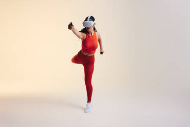 Sportliche junge Frau, die mit 3D-Technologie trainiert. Sportliche junge Frau, die ein Virtual-Reality-Fitnessspiel erkundet. Junge Frau mit Virtual-Reality-Brille in einem Studio. - JLPSF10657