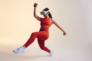 Energetische junge Frau, die mit 3D-Technologie trainiert. Sportliche junge Frau, die ein Virtual-Reality-Fitnessspiel erkundet. Sportliche junge Frau mit Virtual-Reality-Brille in einem Studio. - JLPSF10666