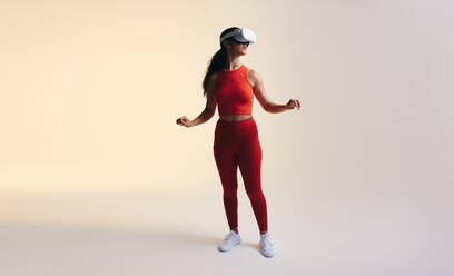 Sportliche junge Frau, die in einem Studio die 3D-Technologie erkundet. Frau, die sich mit einem Virtual-Reality-Headset umsieht. Junge Frau, die ein Virtual-Reality-Spiel betritt. - JLPSF10674