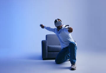 Man playing an immersive virtual reality game in a studio. Young man gaming with virtual reality goggles and controllers. Active young man exploring 3D technology. - JLPSF10698