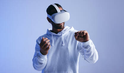 Cheerful young man smiling happily while having an immersive virtual reality experience. Young man looking at his fist through a virtual reality headset. Man enjoying a 3D simulation. - JLPSF10699