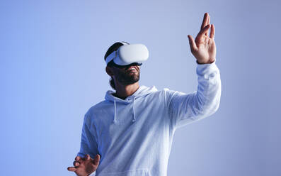 Happy young man touching virtual space with his hand. Cheerful young man experiencing a fun 3D simulation. Young man interacting with the metaverse using virtual reality goggles. - JLPSF10700