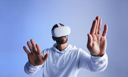 Neugieriger junger Mann, der den virtuellen Raum mit seinen Händen berührt. Junger Mann, der eine 3D-Simulation erlebt. Junger Mann, der mit Hilfe einer Virtual-Reality-Brille mit dem Metaversum interagiert. - JLPSF10701