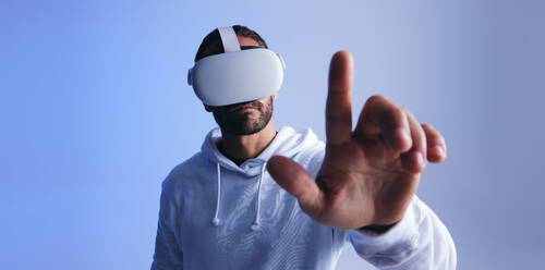 Ein Mann berührt eine Taste im virtuellen Raum. Ein junger Mann interagiert mit dem Metaversum über ein Virtual-Reality-Headset. Ein junger Mann erlebt eine 3D-Simulation. - JLPSF10702