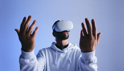 Ein Mann betrachtet seine Hände durch eine Virtual-Reality-Brille in einem Studio. Ein junger Mann erlebt eine 3D-Simulation. Ein junger Mann interagiert mit dem Metaversum. - JLPSF10703