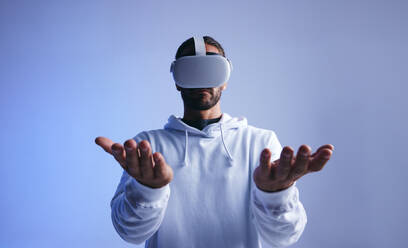 Junger Mann hält seine Hände, während er ein Virtual-Reality-Headset trägt. Junger Mann interagiert mit dem virtuellen Raum im Studio. Mann erlebt eine 3D-Simulation. - JLPSF10704