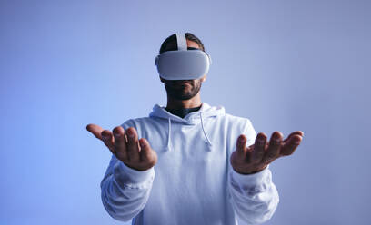 Young man holding his hands while wearing a virtual reality headset. Young man interacting with virtual space in studio. Man experiencing a 3D simulation. - JLPSF10704