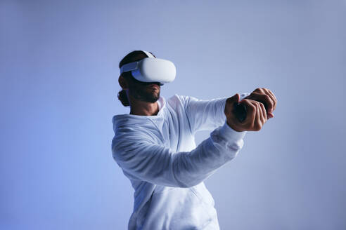 Ein Mann spielt Kricket in der virtuellen Realität. Ein sportlicher junger Mann schlägt einen virtuellen Ball mit Hilfe von Gaming-Controllern. Ein aktiver junger Mann erkundet immersive 3D-Spiele, während er eine Virtual-Reality-Brille trägt. - JLPSF10711