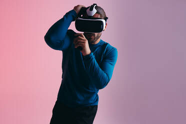 Boxen in der virtuellen Realität. Sportlicher junger Mann, der sich mit einer Virtual-Reality-Brille auf einen virtuellen Schlag vorbereitet. Aktiver junger Mann, der in einem Studio Virtual-Reality-Videospiele ausprobiert. - JLPSF10712