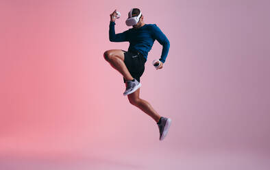 Ein Mann spielt Kickboxen in der virtuellen Realität. Ein aktiver junger Mann springt in der Luft, während er eine Virtual-Reality-Brille trägt. Ein sportlicher junger Mann erkundet immersive Virtual-Reality-Spiele. - JLPSF10720