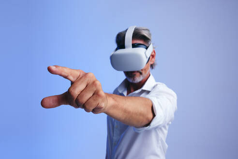 Älterer Geschäftsmann, der mit dem Metaverse interagiert, während er eine Virtual-Reality-Brille trägt. Älterer Geschäftsmann, der mit seinem Finger eine virtuelle Taste drückt. Geschäftsmann, der mit immersiver Technologie arbeitet. - JLPSF10729