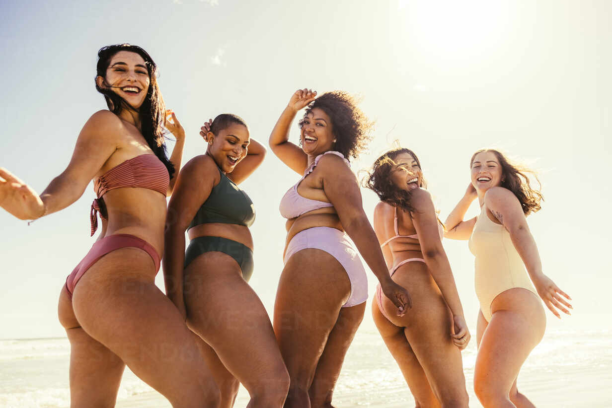 Group of young women dancing together in bikinis. Happy young women smiling  cheerfully while dancing in swimwear. Carefree female friends having fun  and enjoying their summer vacation at the beach. stock photo