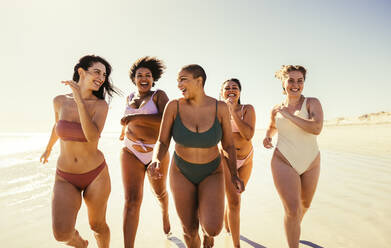 Happy young women running in bikinis at the beach. Group of