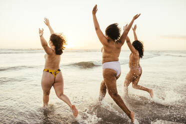 Echter Sommerspaß: Drei junge Frauen, die oben ohne im Wasser planschen und mit erhobenen Armen am Strand laufen. Unbeschwerte Freundinnen, die ihren Urlaub in Bikinihöschen genießen. - JLPSF10788